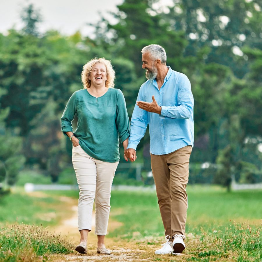 Happy active middle aged white couple having fun walking holding hands and bonding in park outdoors